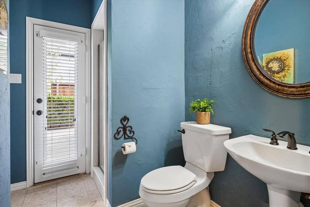 7501 Sweetgum Drive, Irving, TX 75063 Pedestal sink with dark bronze fixtures, white toilet, oval mirror with a decorative frame, and blue textured walls