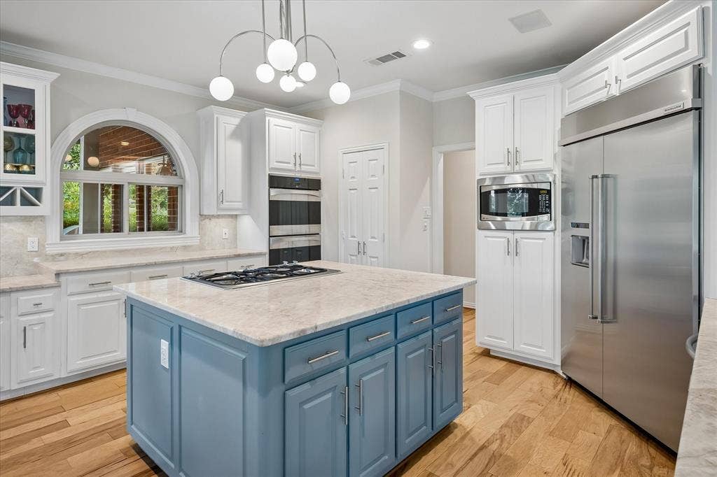 7501 Sweetgum Drive, Irving, TX 75063 Kitchen featuring a central island with gas cooktop, light-toned countertops, white cabinetry, wood-finish flooring, and stainless steel appliances
