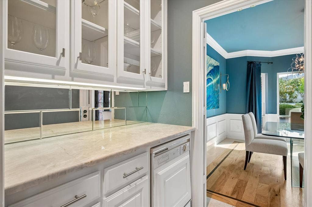 7501 Sweetgum Drive, Irving, TX 75063 Built-in cabinetry with glass-front uppers, light-toned countertop, integrated dishwasher, mirrored tile backsplash, and wide entryway