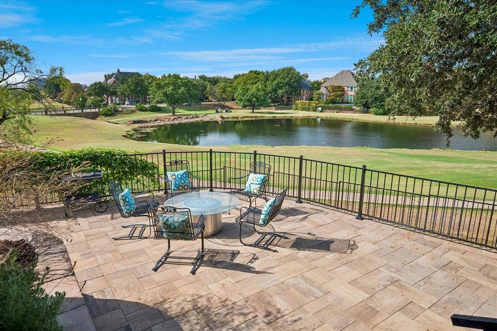 7501 Sweetgum Drive, Irving, TX 75063 Paver patio featuring a wrought iron fence, overlooking a pond and landscaped grounds