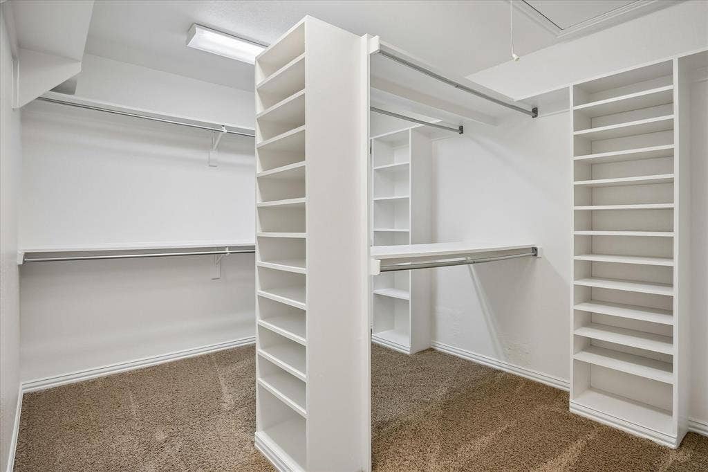 7501 Sweetgum Drive, Irving, TX 75063 Walk-in closet with ample storage, integrated shelving units, multiple clothing rods, and textured carpet flooring
