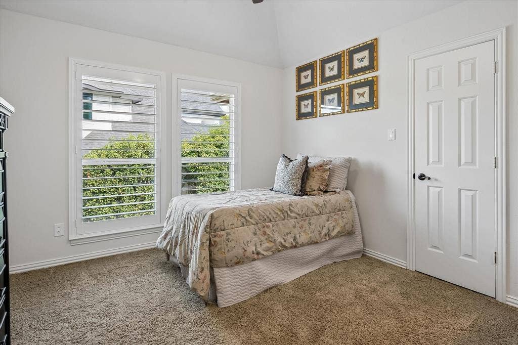 7501 Sweetgum Drive, Irving, TX 75063 Vaulted ceiling, two windows with plantation shutters, paneled door with dark hardware, and neutral carpet flooring
