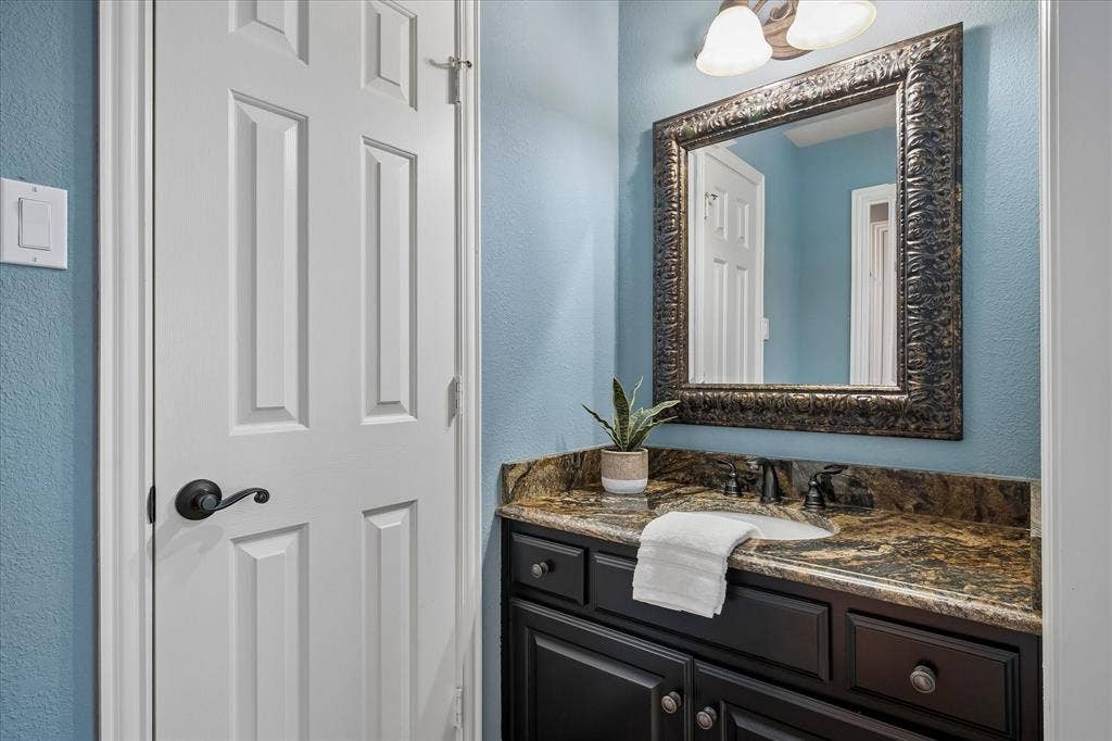7501 Sweetgum Drive, Irving, TX 75063 Built-in vanity with a dark wood-finish cabinet, stone countertop, undermount sink, and dark-toned faucet