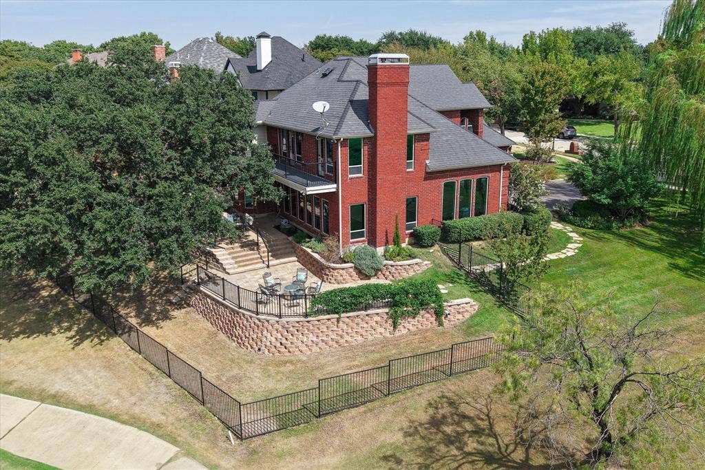 7501 Sweetgum Drive, Irving, TX 75063 Red brick exterior with multiple windows, tiered retaining walls, a stone patio, and a black metal fence
