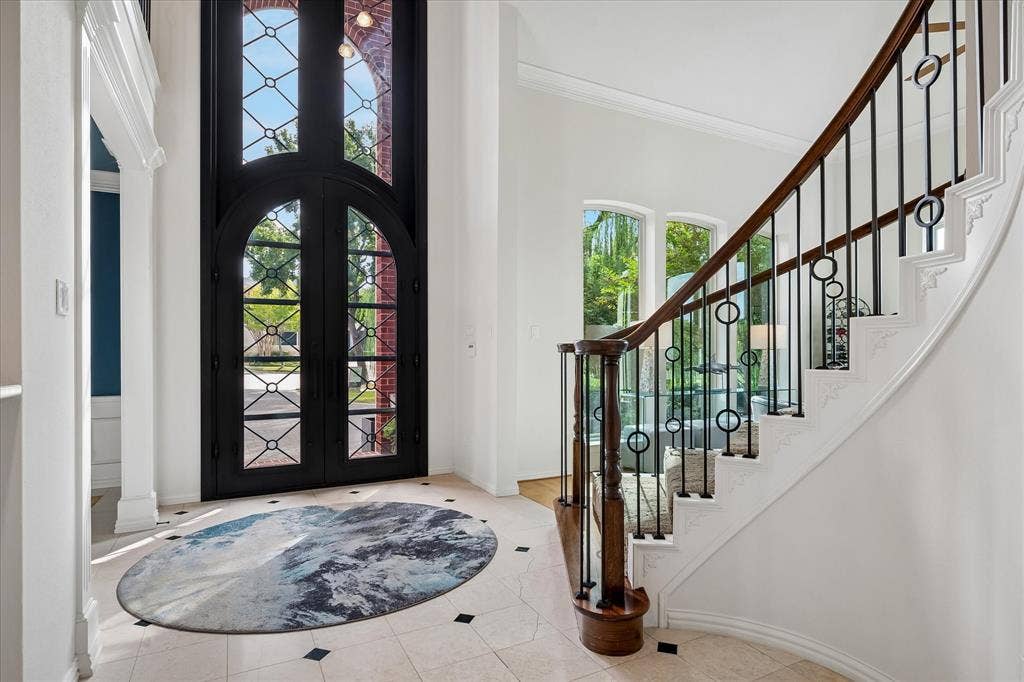 7501 Sweetgum Drive, Irving, TX 75063 Grand entry featuring a curved staircase with decorative wrought iron balusters, a dark wood handrail, and arched windows