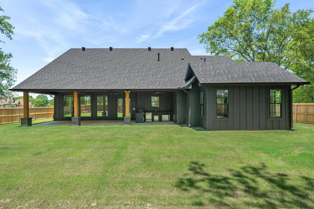 12253 Madison Xing, Bullard, TX 75757 Expansive backyard with a manicured lawn, featuring a covered patio, outdoor kitchen, and dark gray board and batten siding