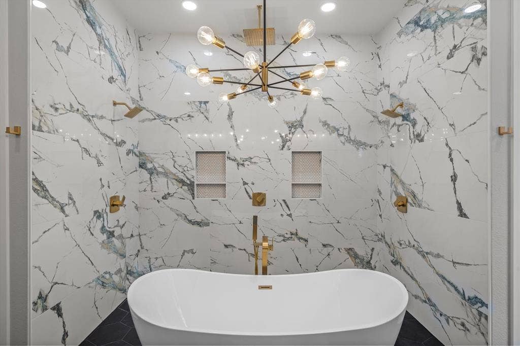 12253 Madison Xing, Bullard, TX 75757 Freestanding soaking tub centered within a spacious wet room featuring large format marble-look tile walls, dual gold-finish rain shower heads, and built-in tiled shower niches