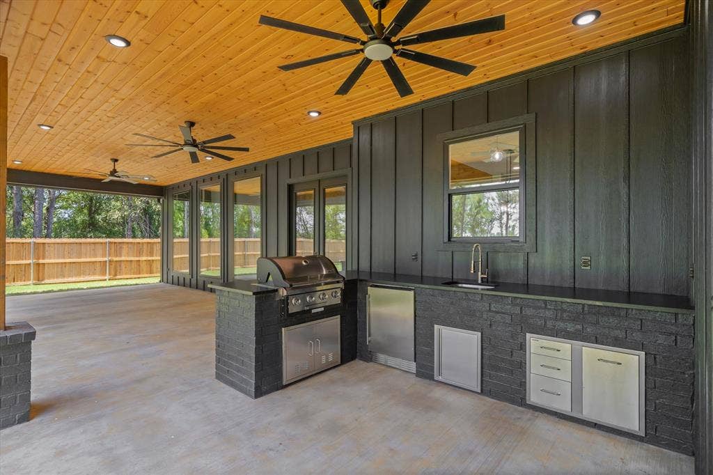 12253 Madison Xing, Bullard, TX 75757 Spacious covered patio featuring a wood-panel ceiling with recessed lighting, an outdoor kitchen with stainless steel appliances, a built-in grill, and a black brick island with a sink and countertop