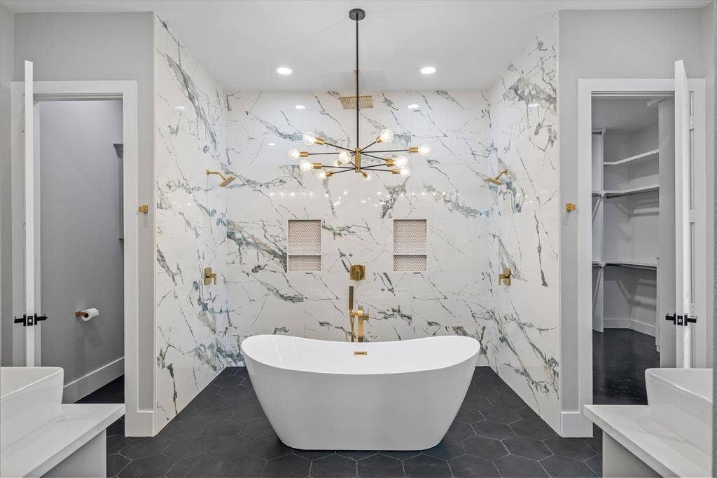 12253 Madison Xing, Bullard, TX 75757 Freestanding soaking tub centered in a spacious bathroom featuring patterned wall tile, dark hexagonal floor tile, and a contemporary chandelier