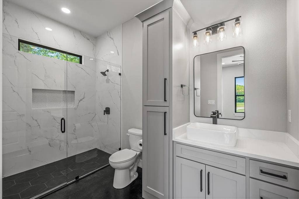 12253 Madison Xing, Bullard, TX 75757 Contemporary bathroom featuring a spacious walk-in shower with white marble-look tile, black hexagonal floor tile, and a transom window