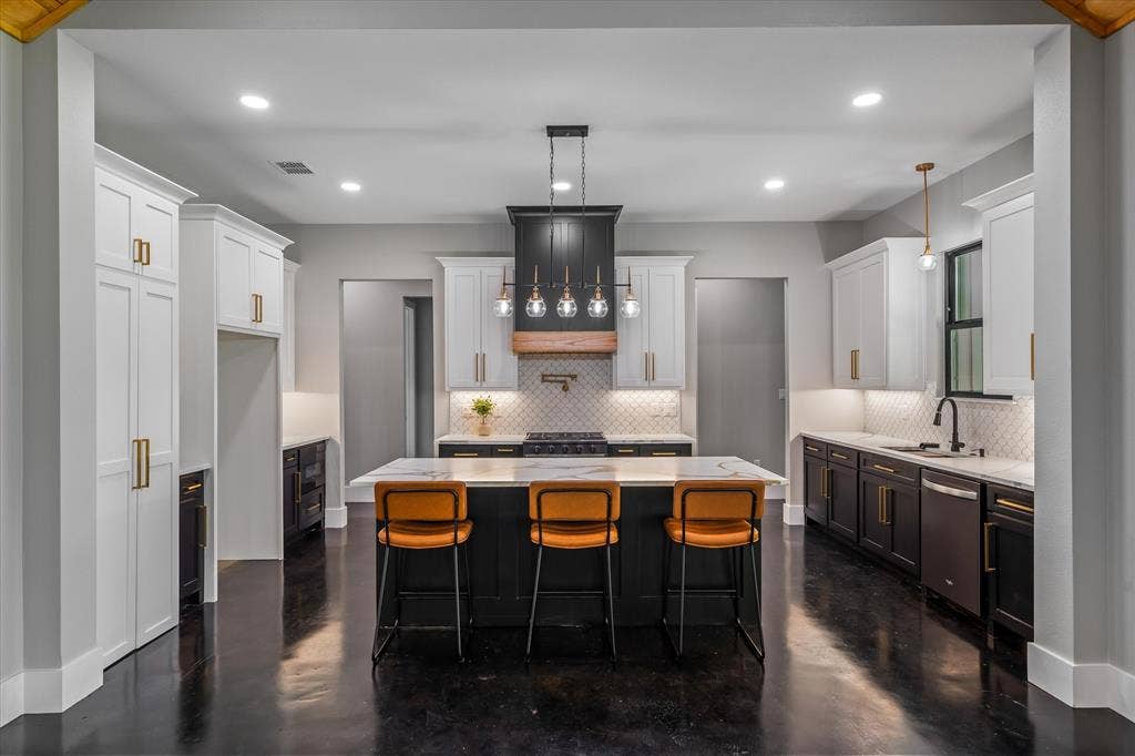 12253 Madison Xing, Bullard, TX 75757 Spacious kitchen featuring a central island with countertop seating, white and dark-toned cabinetry with gold-finish hardware, stainless steel appliances, and a tile backsplash