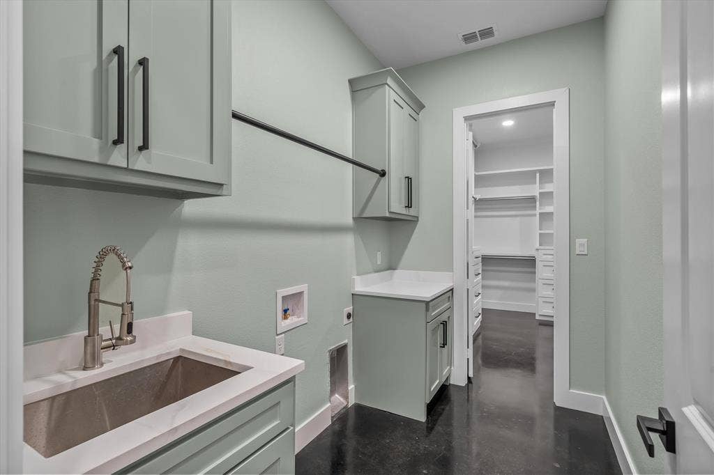12253 Madison Xing, Bullard, TX 75757 Laundry area featuring light green cabinetry with matte black hardware, a stainless steel sink with a gooseneck faucet, white solid surface countertops, and a clothes hanging rod
