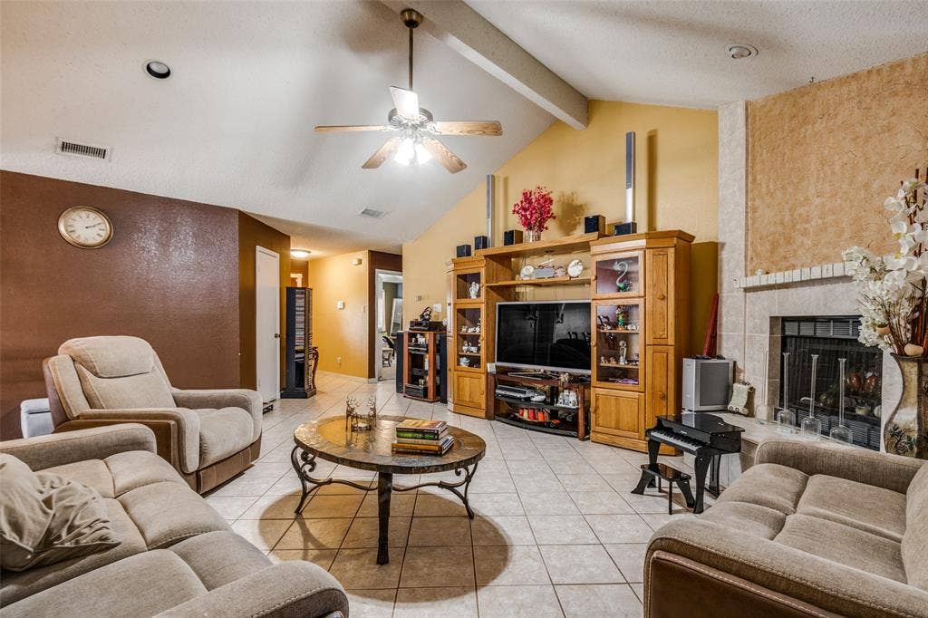 Vaulted ceiling with exposed beam, tile flooring, built-in entertainment center, and a brick-surround fireplace with hearth