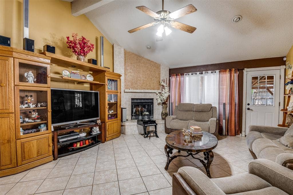 Vaulted ceiling with a ceiling fan, fireplace with a stone surround, tiled flooring, and a paneled entry door with glass inserts