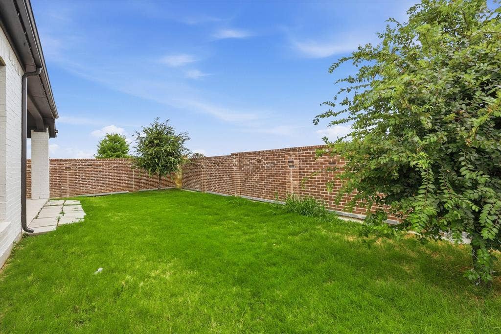 787 Cedarwood Court, Haslet, TX 76052 Spacious grassy yard featuring a brick perimeter wall, mature trees, and a flagstone patio area