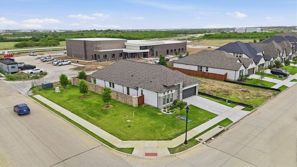 787 Cedarwood Court, Haslet, TX 76052 Corner lot residence featuring a light-colored stucco exterior, a dark shingle roof, an attached garage, a concrete driveway, and a verdant lawn with newly planted trees