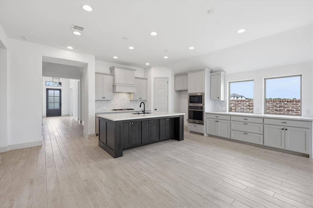 787 Cedarwood Court, Haslet, TX 76052 Open-concept kitchen featuring wood-finish flooring, a central island with dark cabinetry, light-toned perimeter cabinetry, integrated stainless steel appliances, and multiple windows