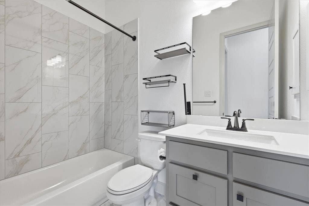 787 Cedarwood Court, Haslet, TX 76052 Bathroom featuring a white bathtub, large format tile surround with marble-look veining, gray vanity with dark hardware, white countertop with integrated sink, and dark-finished faucet
