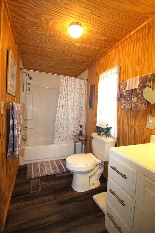 921 Crown Drive, Tool, TX 75143 Bathroom featuring wood-paneled walls and ceiling, dark wood-finish flooring, a white bathtub with shower, a white toilet, and a white vanity with drawers