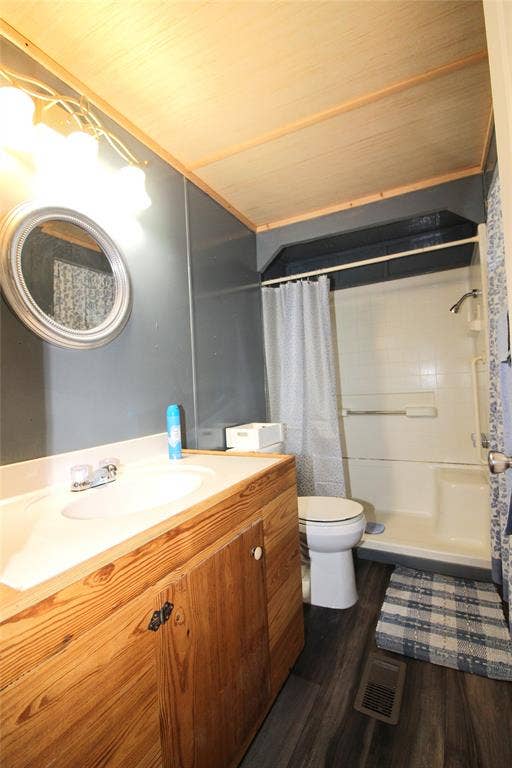921 Crown Drive, Tool, TX 75143 Bathroom featuring a wood-finish vanity with an integrated sink, a circular framed mirror, wood-finish flooring, a shower-tub combination, and a wood-panel ceiling