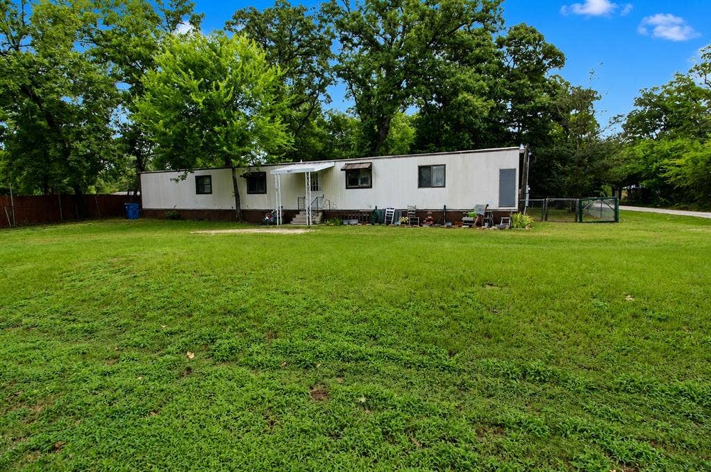 921 Crown Drive, Tool, TX 75143 Expansive green lawn surrounds the property, featuring a white mobile home with dark trim windows and a covered entry porch