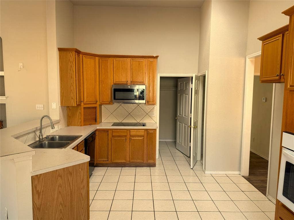 Kitchen featuring wood cabinetry, white tile flooring, stainless steel microwave, and a double basin sink