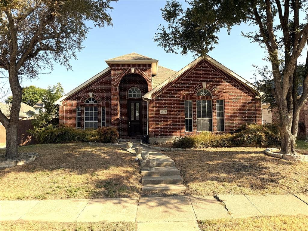 Brick facade with arched entry, complementing arched windows, and mature trees