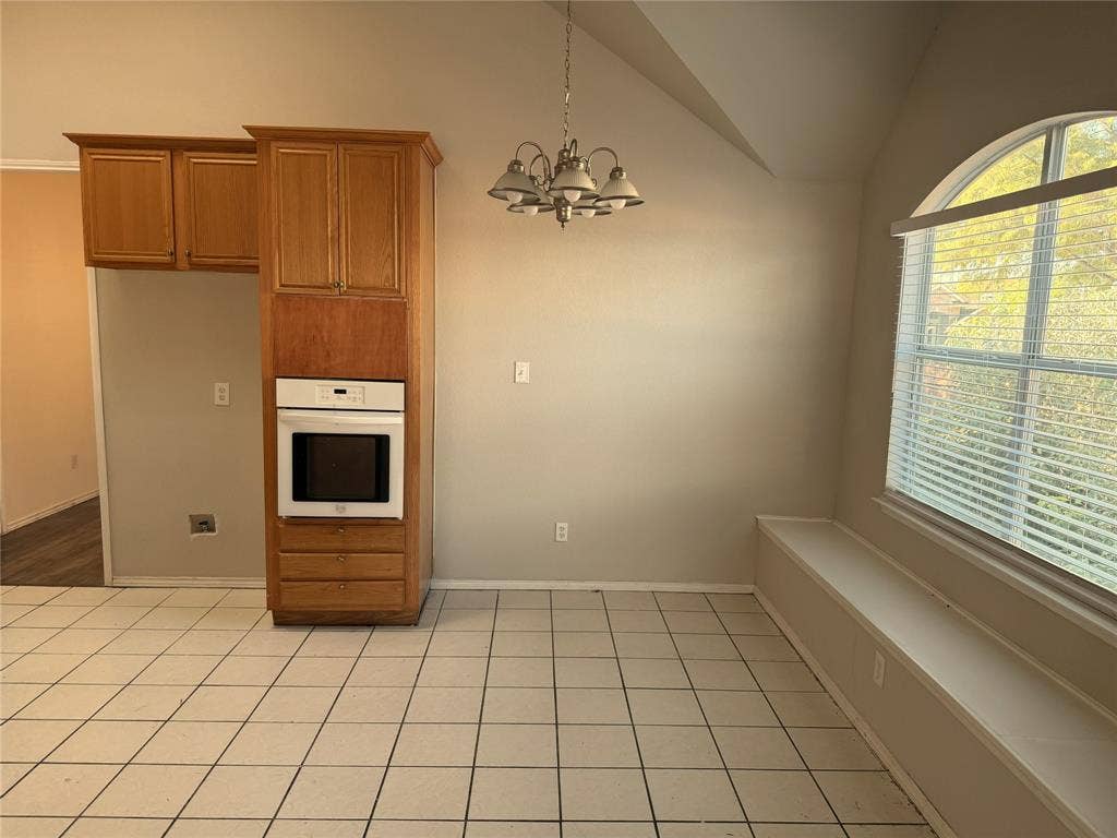 Built-in cabinetry with integrated oven, tiled flooring, arched window, built-in bench seating, and ceiling chandelier