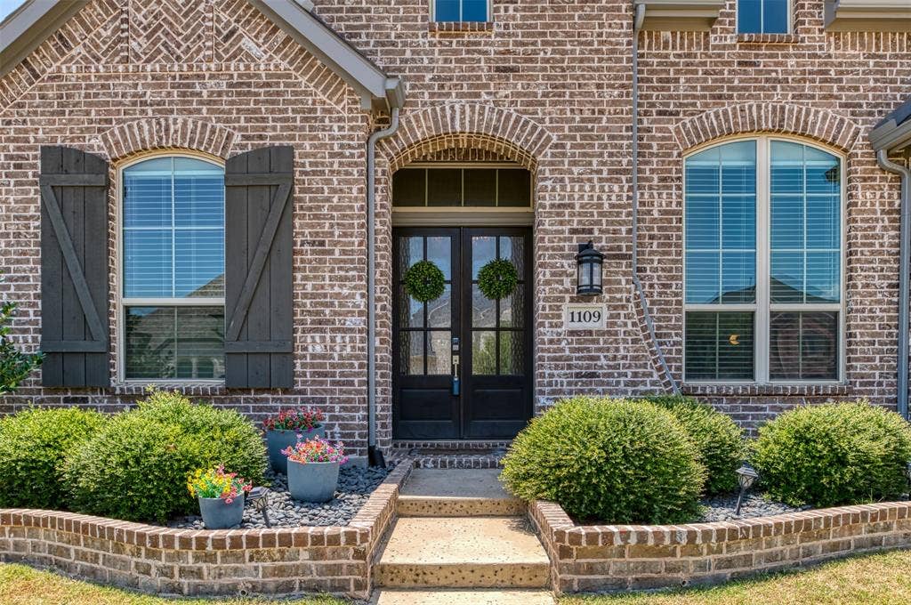 1109 10th Street, Argyle, TX 76226 Brick exterior featuring arched window headers, a dual-pane arched entry door, and dark wood shutters