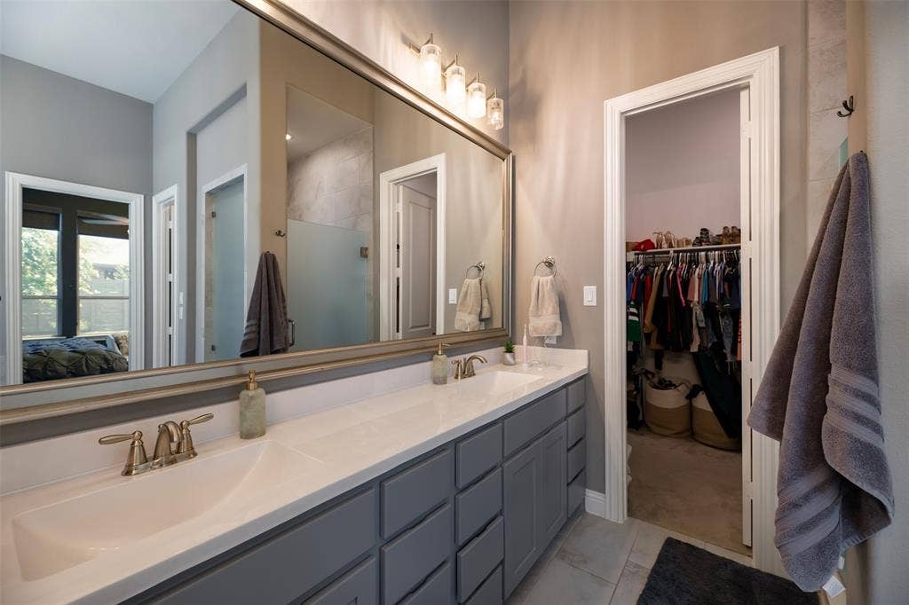 1109 10th Street, Argyle, TX 76226 Bathroom vanity featuring dual sinks, a large framed mirror, gray cabinetry, and brass-finish fixtures