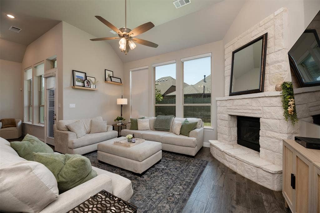 1109 10th Street, Argyle, TX 76226 Spacious living area featuring a stone-clad fireplace with hearth, vaulted ceilings, a ceiling fan with integrated lighting, and wood-finish flooring