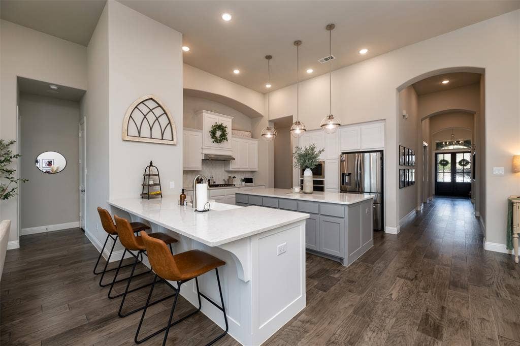 1109 10th Street, Argyle, TX 76226 Open-concept kitchen featuring an eat-at island with a quartz countertop, recessed lighting, wood-finish flooring, and arched doorways