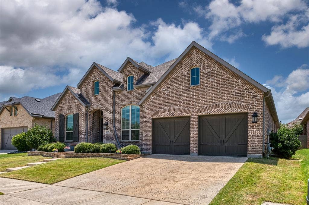 1109 10th Street, Argyle, TX 76226 Brick exterior featuring a two-car garage with carriage-style doors, arched window accents, gabled rooflines, and a concrete driveway