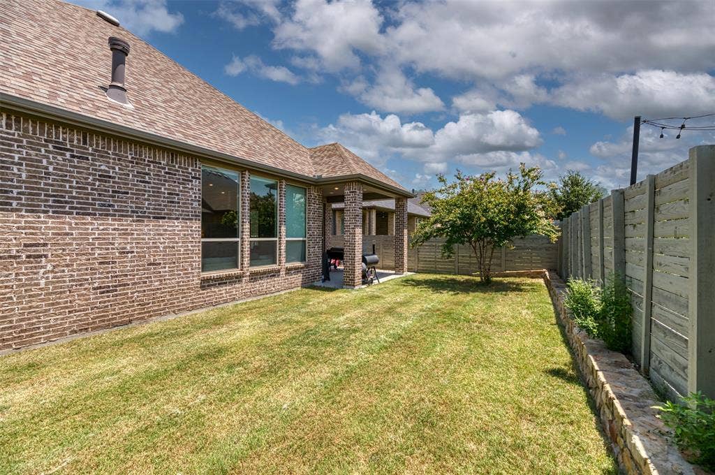 1109 10th Street, Argyle, TX 76226 Expansive backyard with a manicured lawn, a mature tree, and a stone retaining wall