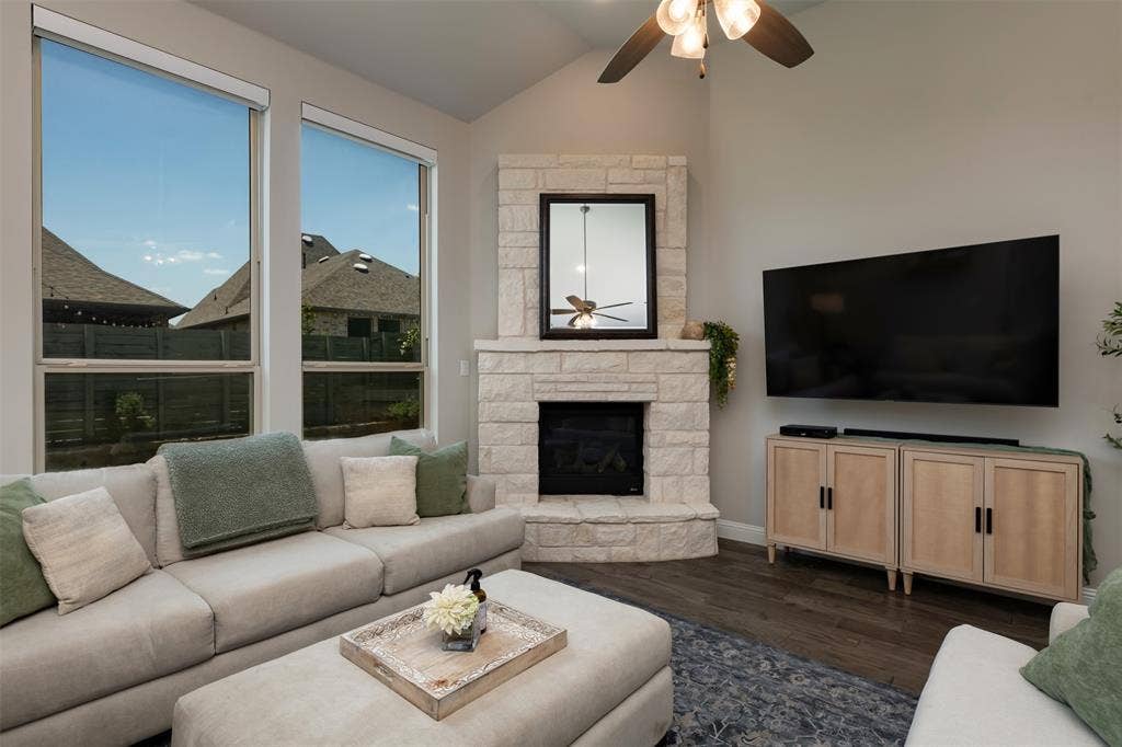 1109 10th Street, Argyle, TX 76226 Living area featuring a stone-clad fireplace, dark wood-finish flooring, and a vaulted ceiling with a ceiling fan