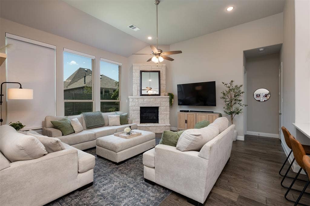 1109 10th Street, Argyle, TX 76226 Spacious living area featuring high vaulted ceilings, large windows with roller shades, a stone-clad corner fireplace, and wood-finish flooring