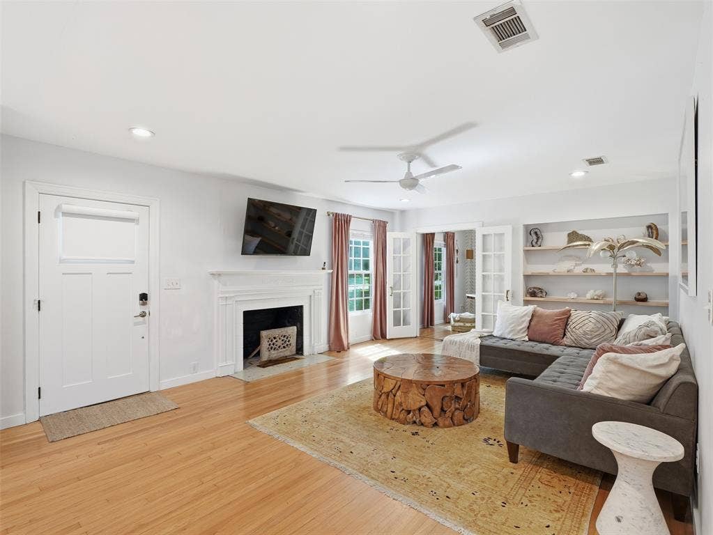 Living room featuring wood-finish flooring, a fireplace with a white mantel, and built-in shelving