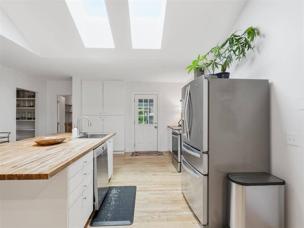 Modern kitchen featuring a large butcher block island with undermount sink, stainless steel appliances, and white cabinetry