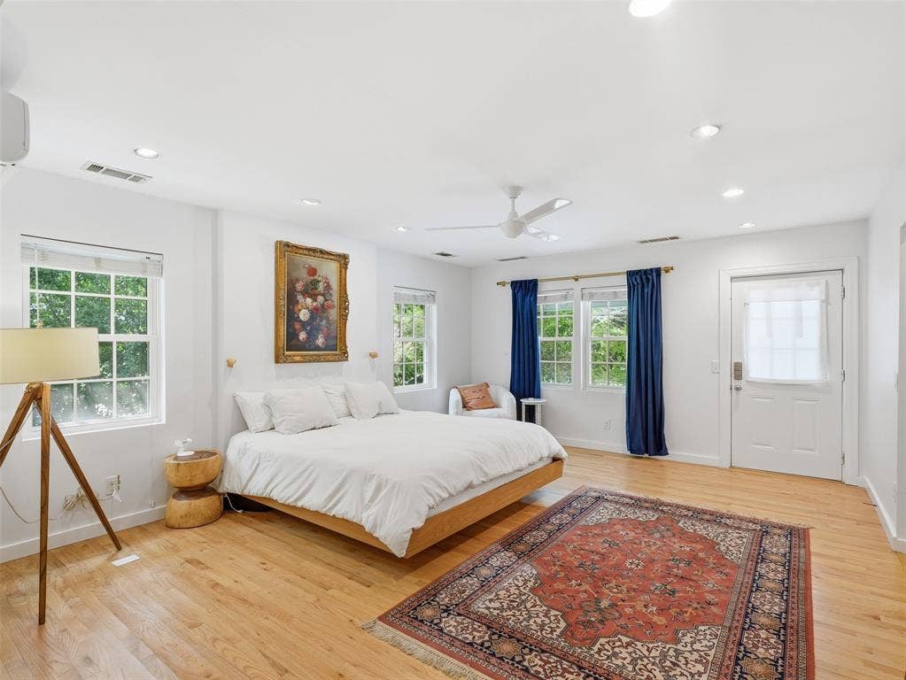 Bright bedroom featuring light wood-finish flooring and multiple windows with white blinds
