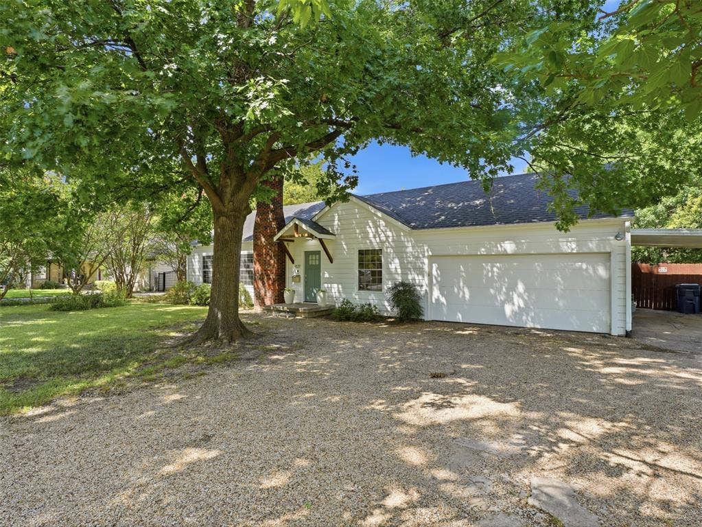 White exterior residence featuring a front gravel driveway and a mature shade tree