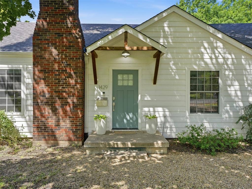 White siding exterior featuring a covered entry, a teal front door with upper lites, a substantial brick chimney, and a gravel front yard