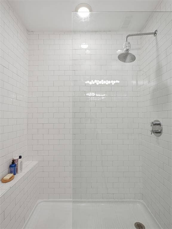 Tiled shower enclosure featuring white subway tile walls, a built-in shelving niche, a clear glass panel, and a wall-mounted showerhead with control fixtures