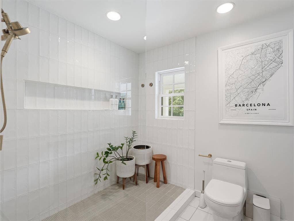 Walk-in shower featuring a built-in niche, white rectangular tile walls, a rain shower head, and light-toned floor tile