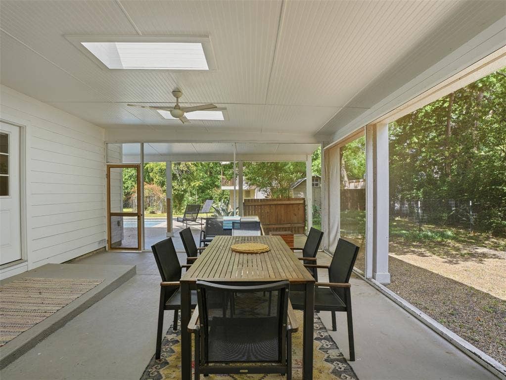Screened porch with two skylights, a ceiling fan, a screened door, and concrete flooring