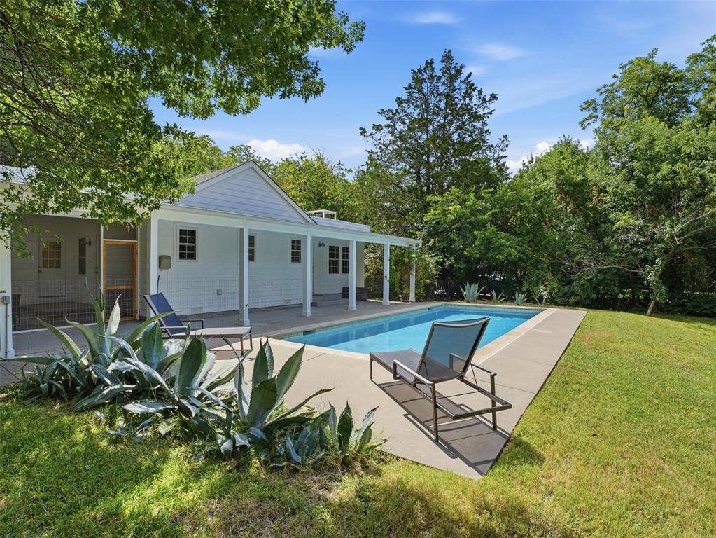Rectangular swimming pool with a surrounding concrete deck, bordered by a manicured lawn and mature trees