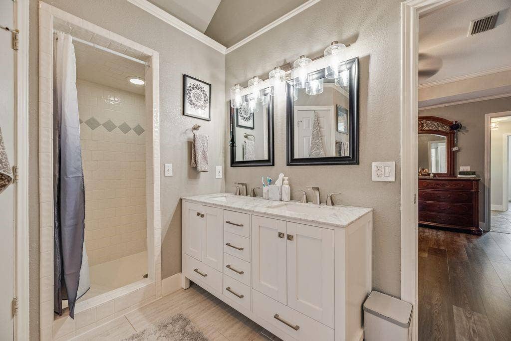 419 N Winding Oaks Drive, Wylie, TX 75098 Bathroom featuring a double vanity with white cabinetry and a light-toned countertop, dual rectangular mirrors, and a shower with subway tile surround and decorative accents
