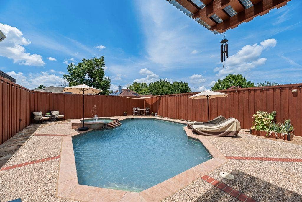 419 N Winding Oaks Drive, Wylie, TX 75098 Private backyard featuring an in-ground swimming pool with an integrated spa, exposed aggregate concrete decking with brick accents, and a perimeter privacy fence