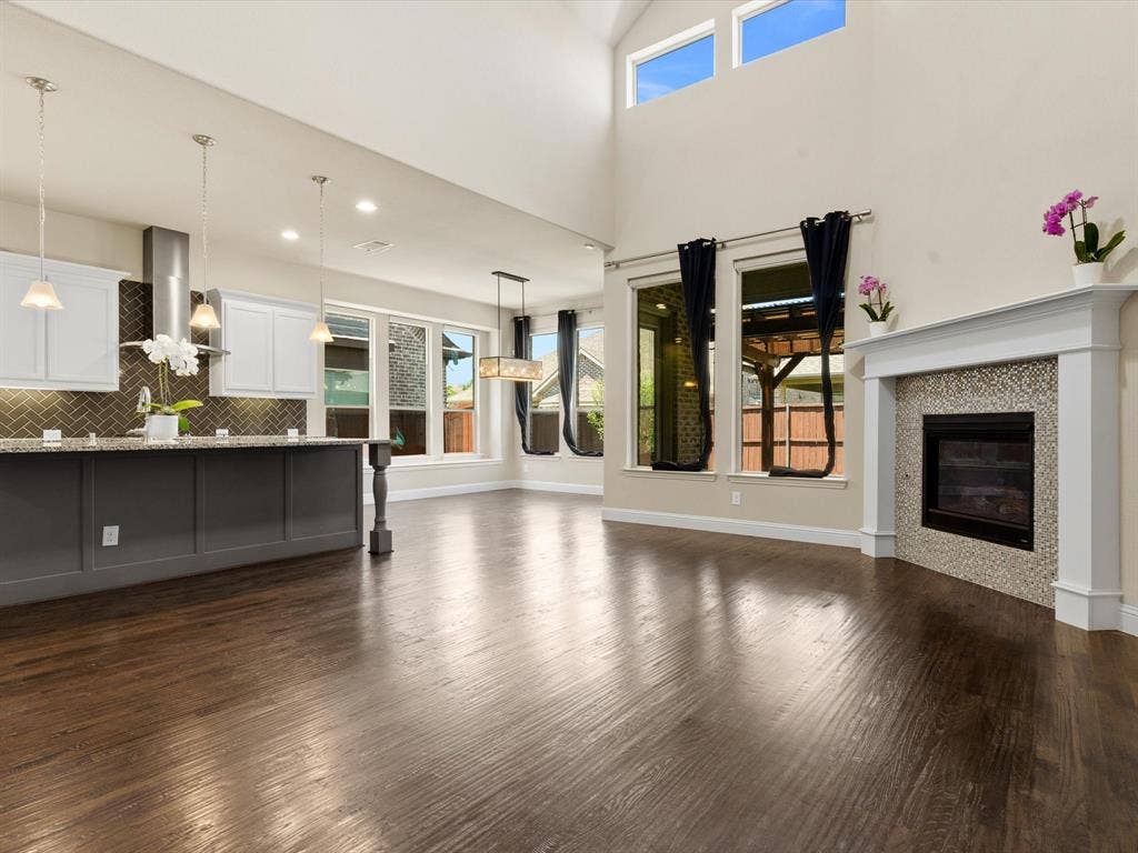 2703 Navarro Trail, Euless, TX 76039 Open-concept living space with dark wood-finish flooring, a two-story vaulted ceiling, and a fireplace featuring a mosaic tile surround