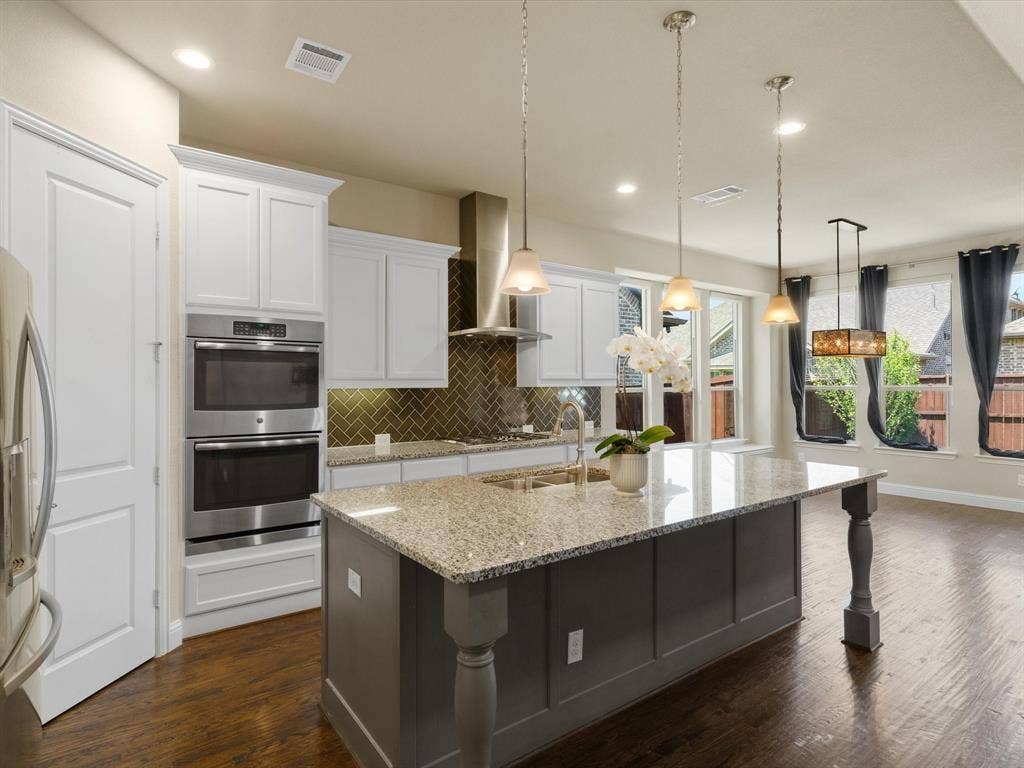 2703 Navarro Trail, Euless, TX 76039 Kitchen featuring a large island with granite countertop, stainless steel double ovens, herringbone pattern backsplash, white cabinetry, and wood-finish flooring