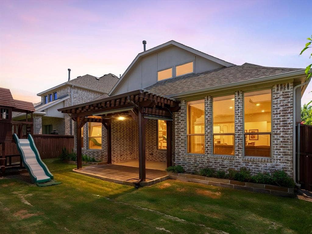 2703 Navarro Trail, Euless, TX 76039 Expansive backyard featuring a covered patio with a dark wood pergola, a brick exterior, multiple large windows, and a green lawn